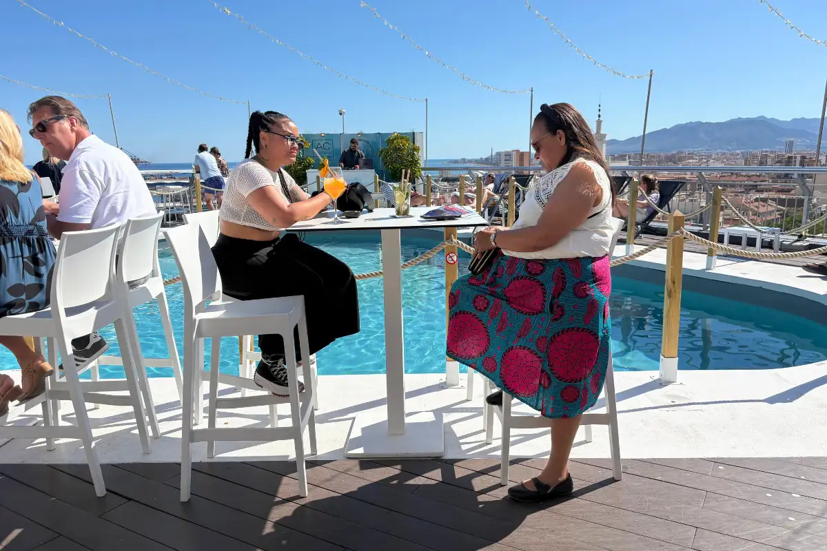 People chatting at pool-edge tables with mountain views at AC Hotel Malaga Palacio
