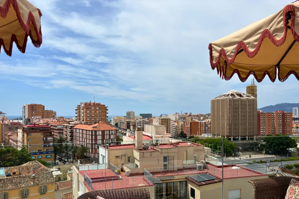 Malaga city rooftops and hills seen past a fringed parasol at H10 Croma