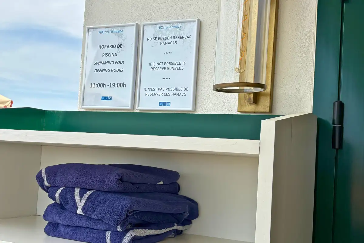 Folded blue towels and pool opening hours sign at H10 Croma, Malaga
