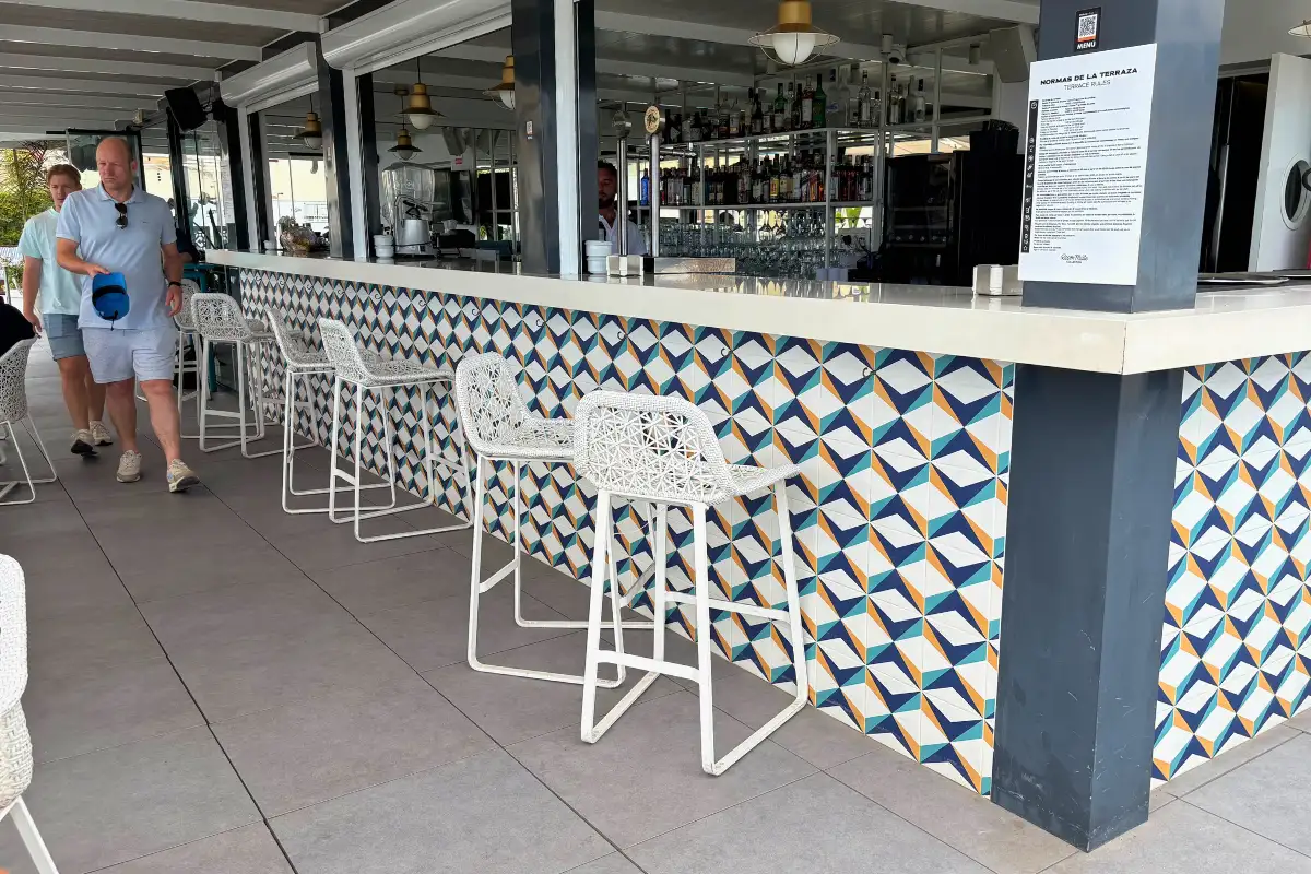 Blue and yellow tiled bar counter with white stools at La Terraza de Valeria in Malaga