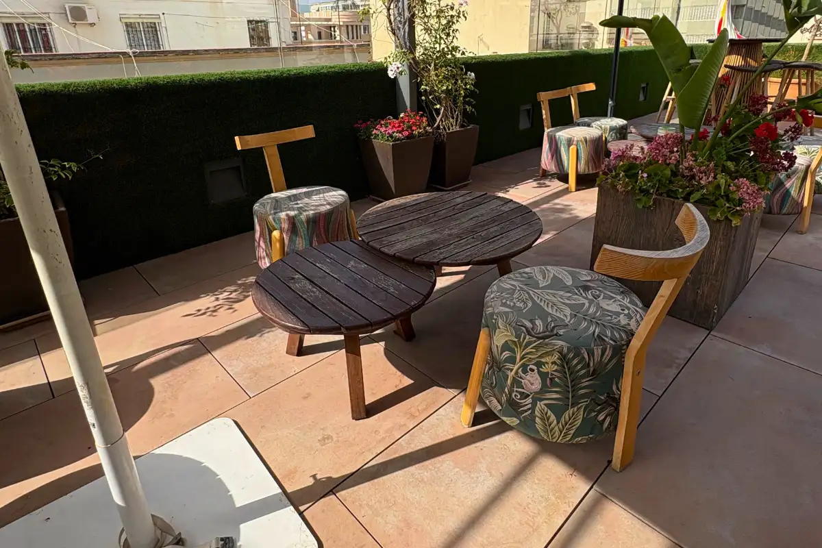 Round wooden table with cushioned stools on the terrace at EFECTO Rooftop, Hotel Mariposa Malaga