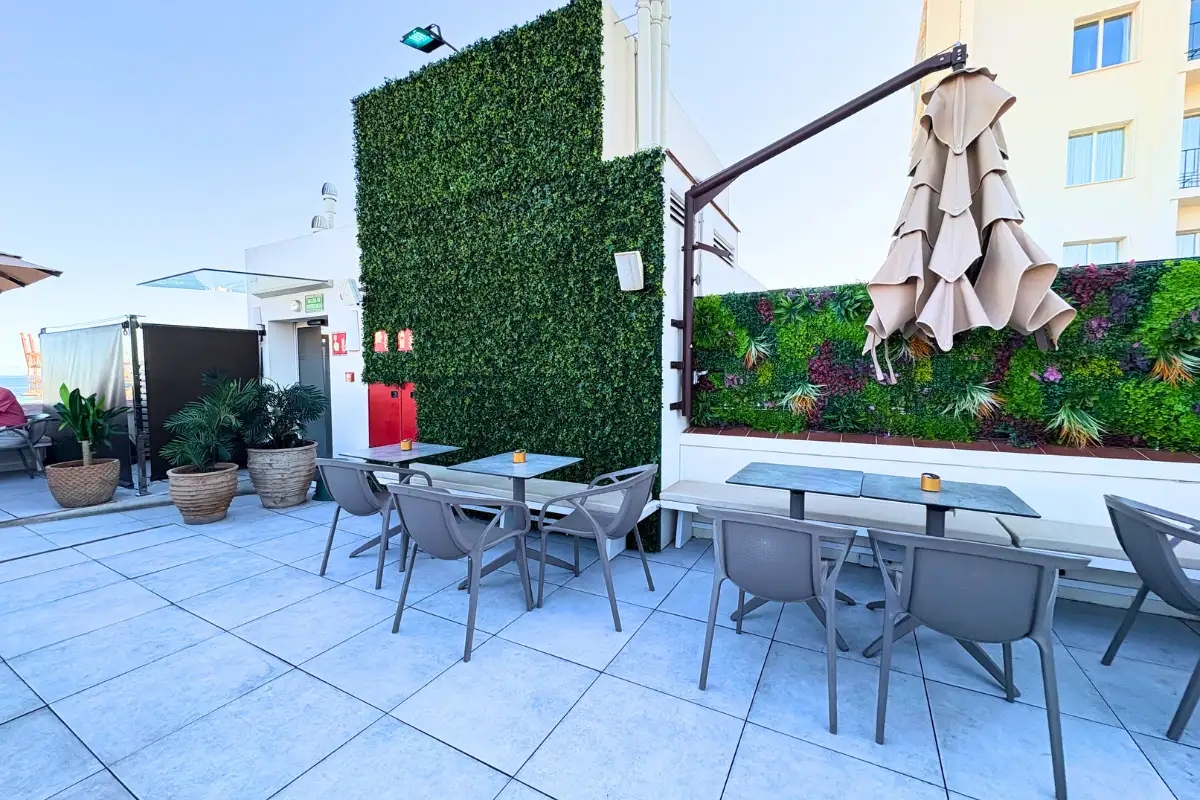 Dining tables along a green hedge wall on the terrace at Lolita Skyview in Malaga
