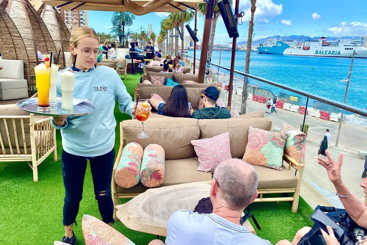 Server carrying cocktails through the beachfront lounge seating at Nusa, Malaga
