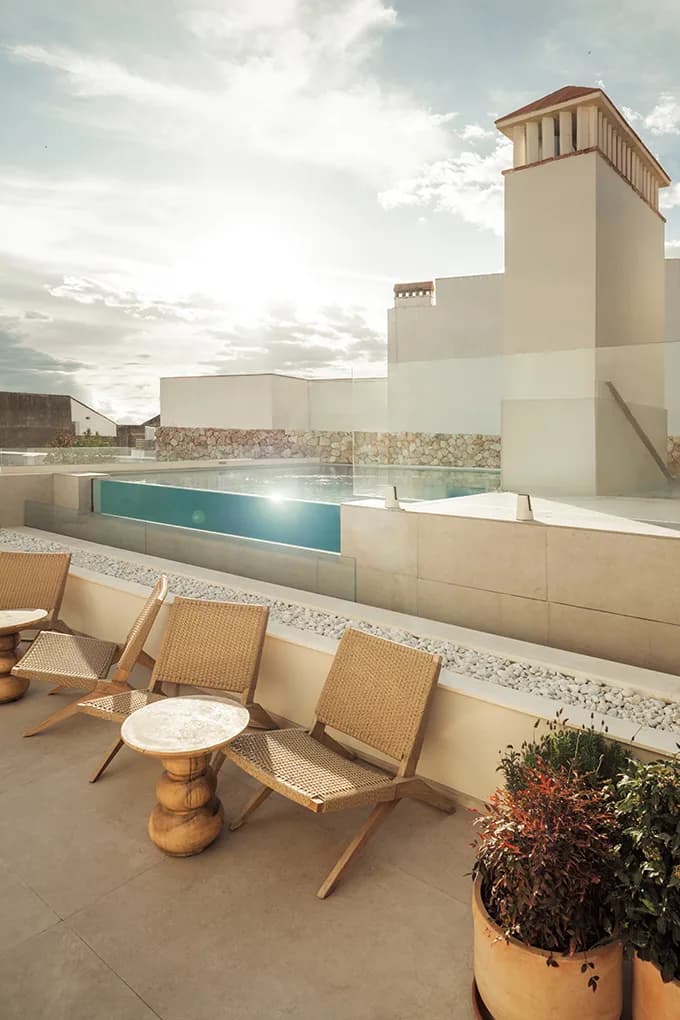 Woven lounge chairs beside the rooftop pool at Well and Come with an old town chimney behind