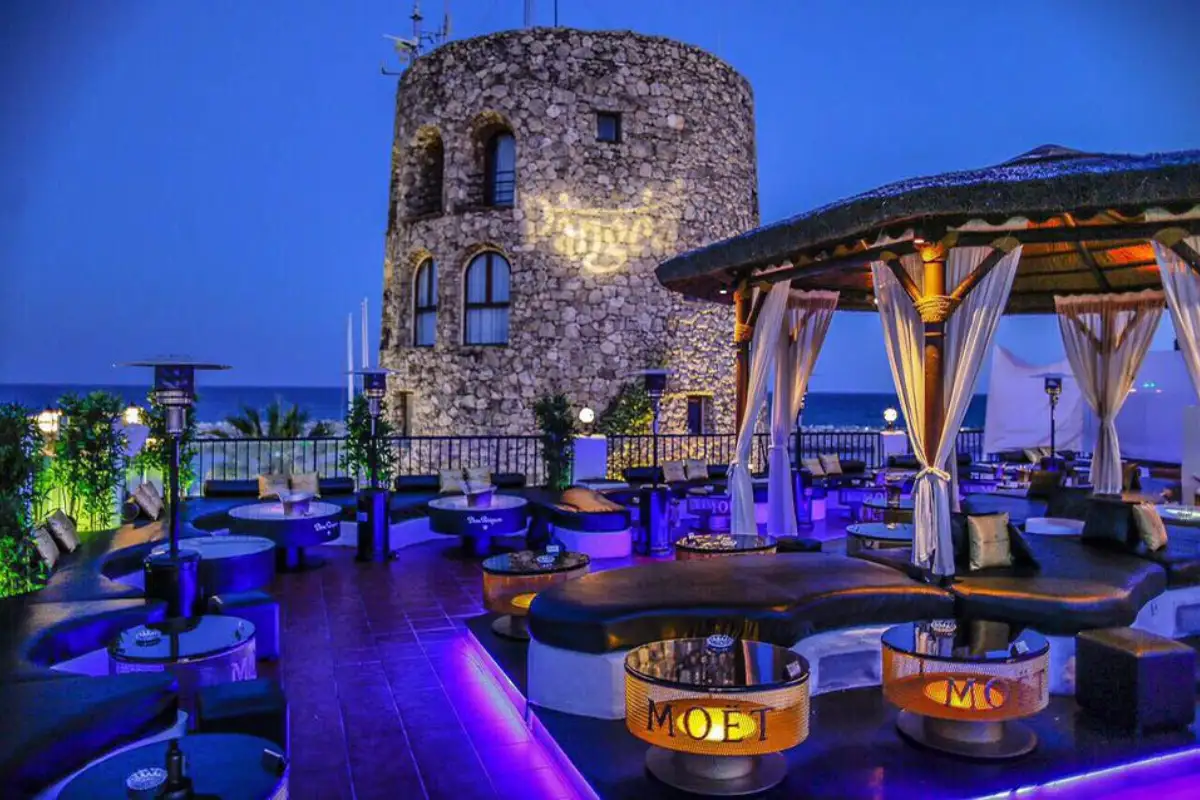Stone tower and lit lounge seating at night at Pangea rooftop, Marbella