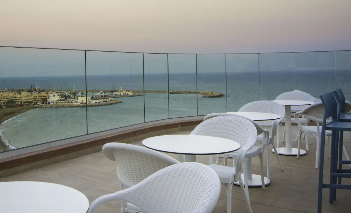 White tables by a glass balustrade with sea and marina views at Celeste Skybar, Benalmadena
