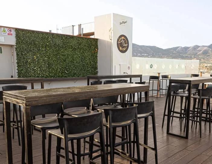 High wooden tables and stools with mountain backdrop at Sky Bar Veramar, Fuengirola