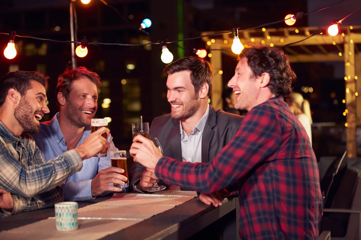 Group of men laughing over drinks at an evening rooftop bar in Malaga