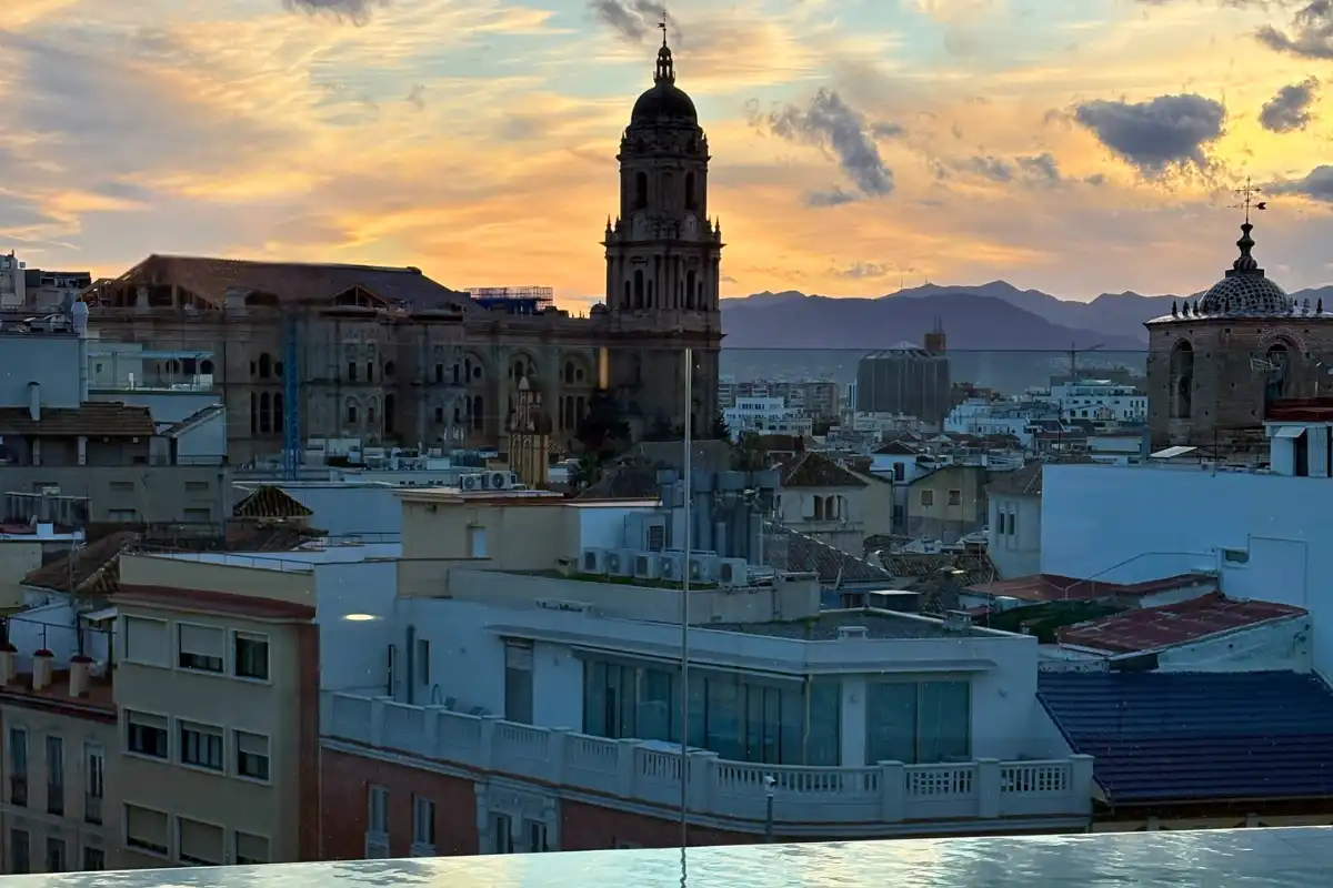 Malaga cathedral tower silhouetted against a glowing sunset over the city rooftops at ME Malaga