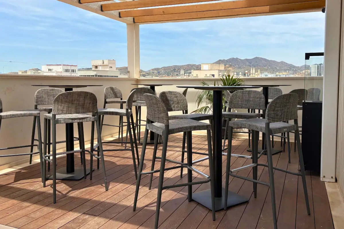 High bar tables under a pergola with mountain views at Soho Boutique Equitativa rooftop in Malaga