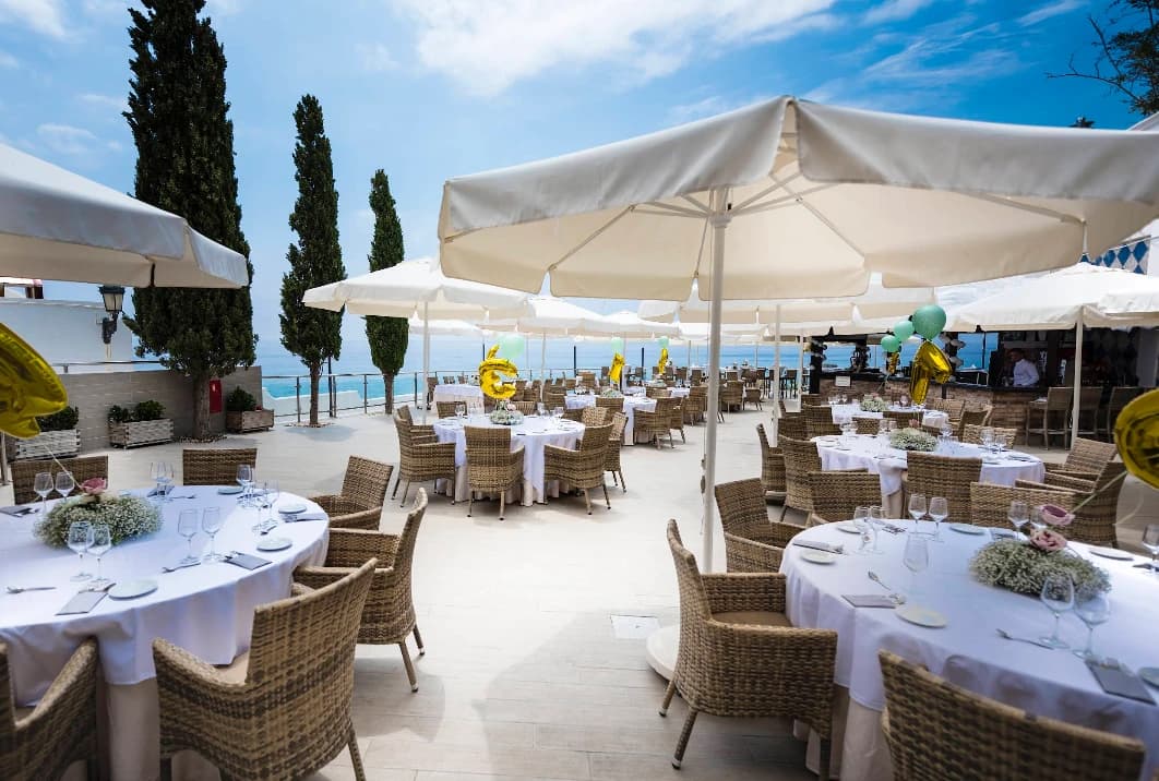 White-clothed dining tables under parasols by the sea at Cochran's Terrace, Nerja