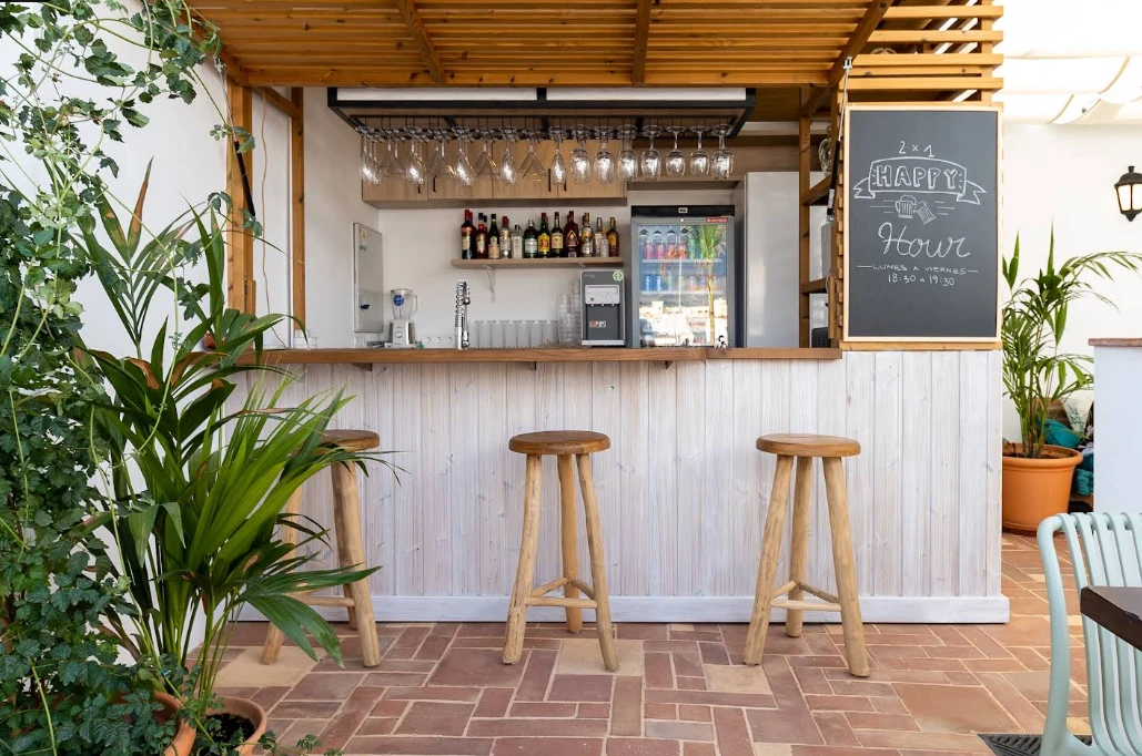 Rustic wooden honesty bar with stools and plants on the rooftop at Hostel Veranera, Estepona