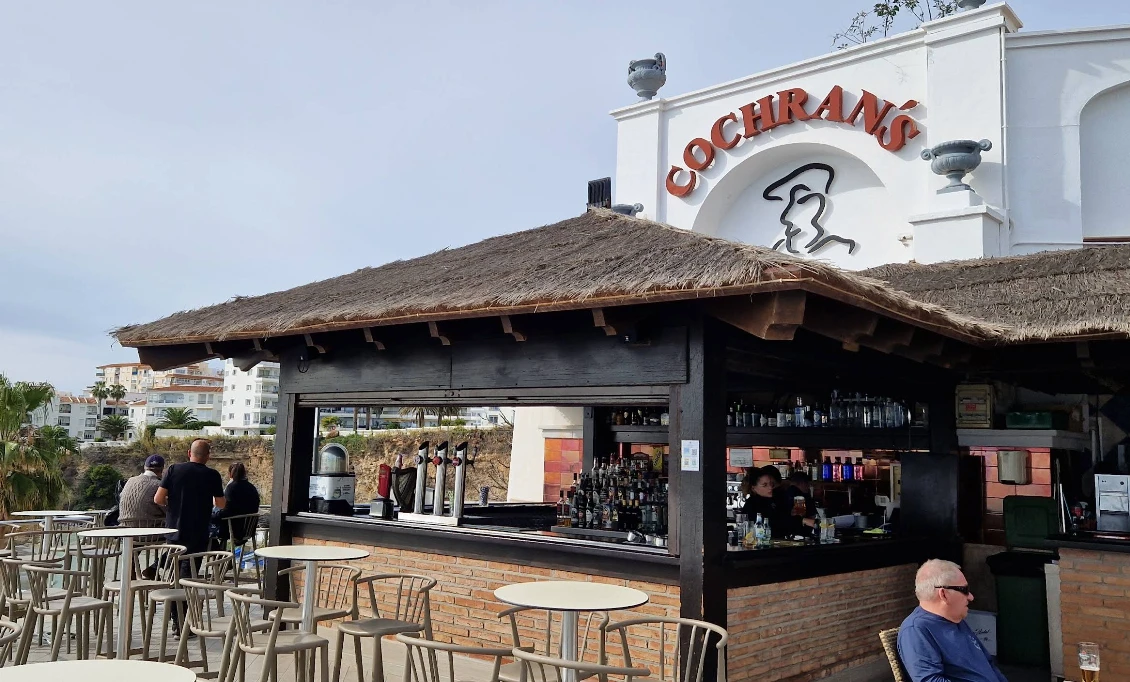 Thatched-roof bar exterior with outdoor tables at Cochran's Terrace, Nerja